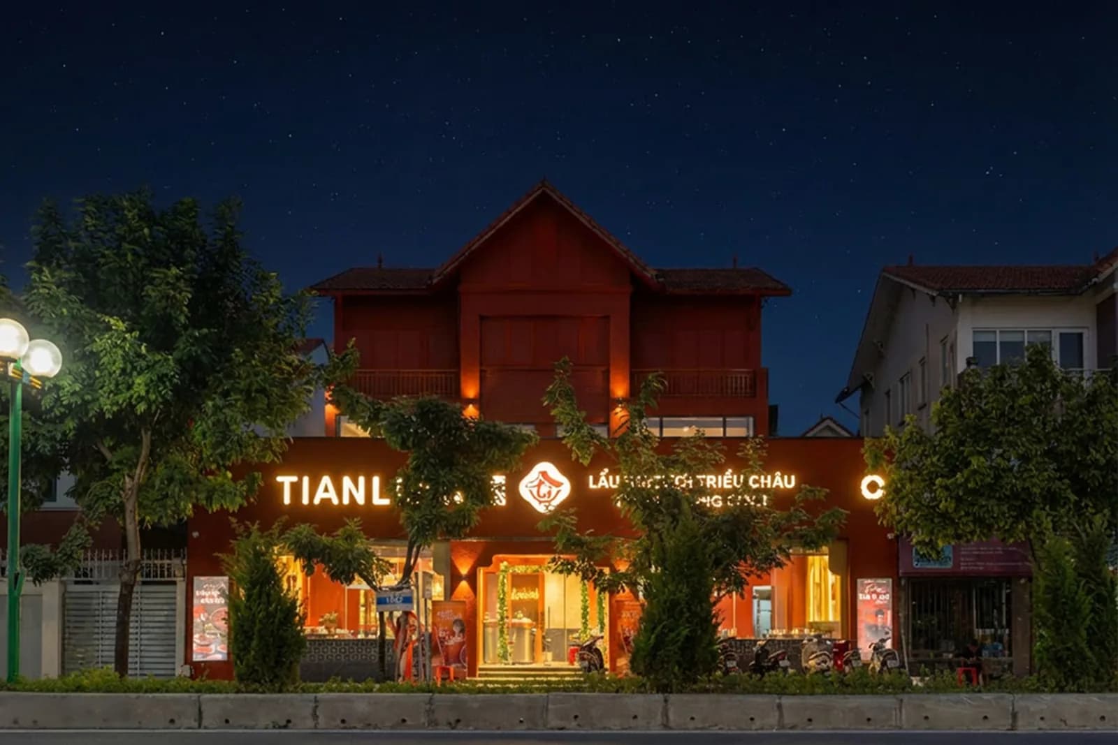 Nhà hàng Tian Long ở Vũ Trọng Khánh, Hà Đông: tòa nhà hai tầng ốp gỗ sơn đỏ, mái ngói dốc, biển hiệu chạy suốt mặt tiền, đèn vàng hắt ra từ bên trong lúc chạng vạng